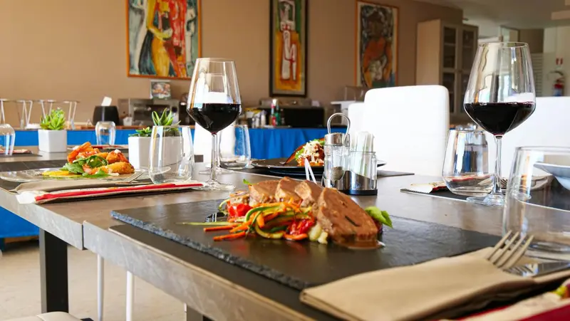 Une table est dressée avec des plats et des verres de vin dans une salle lumineuse.