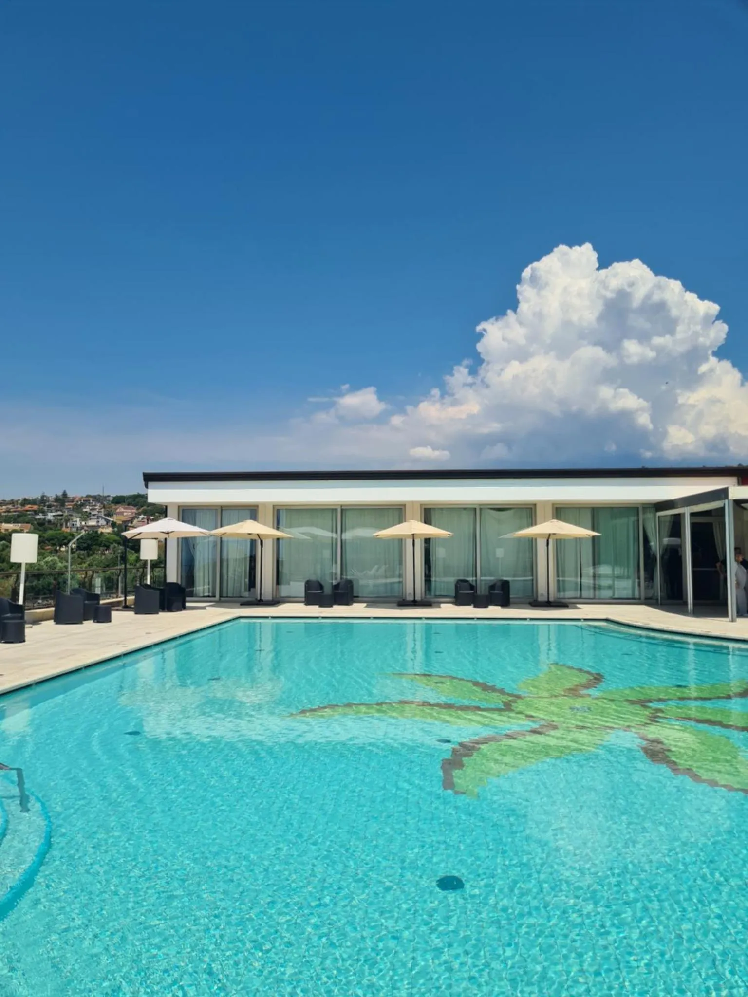 Une piscine turquoise avec un motif floral au fond, bordée de transats et de parasols.