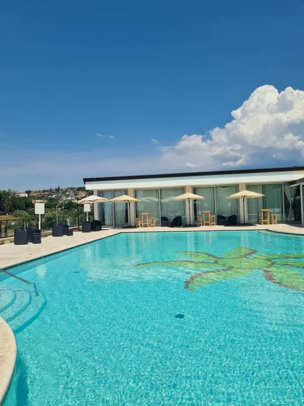 Une piscine turquoise avec un motif de feuille au fond, entourée d'une terrasse avec des parasols.