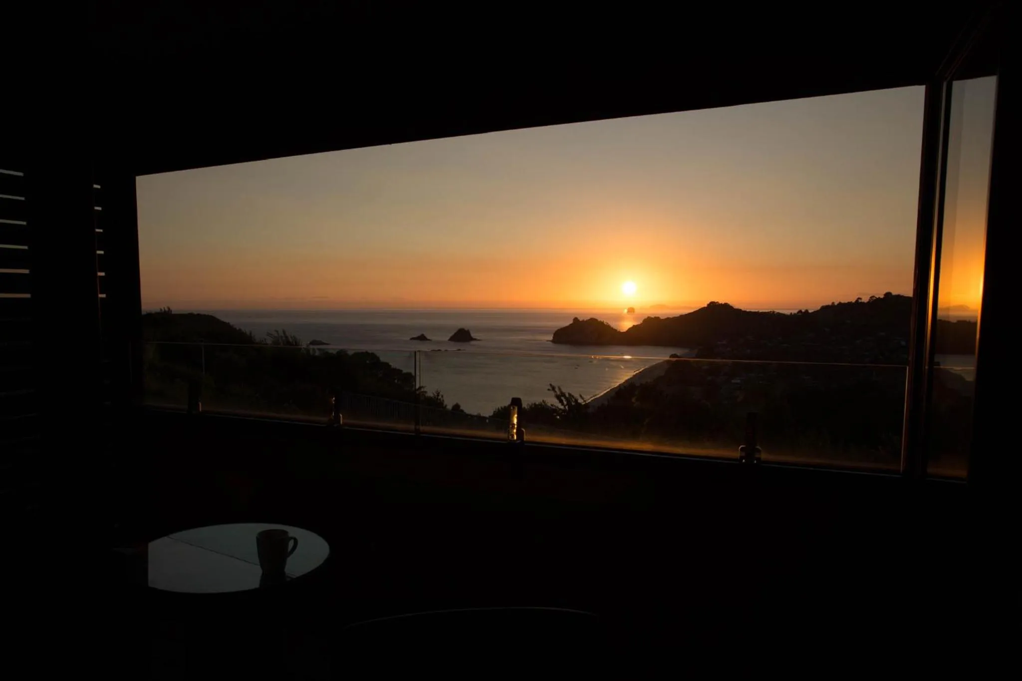 Vue sur la mer et le soleil couchant depuis une fenêtre sombre.