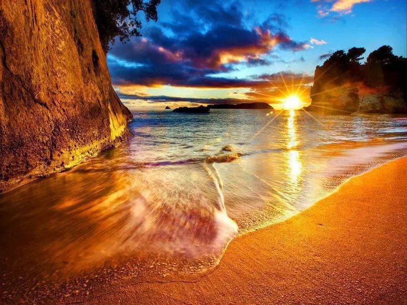 Le soleil se couche sur une plage de sable doré, illuminant les vagues et les falaises.