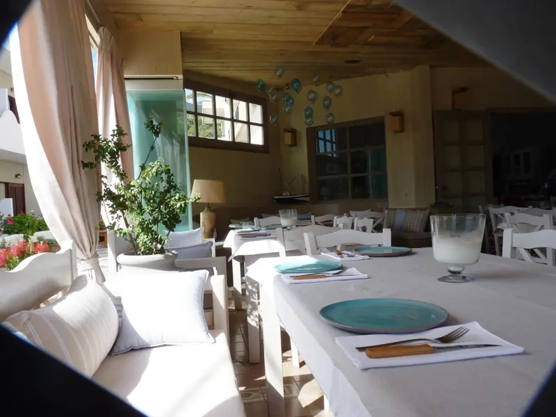 Une table est dressée avec de la vaisselle et des couverts sur une terrasse ombragée.