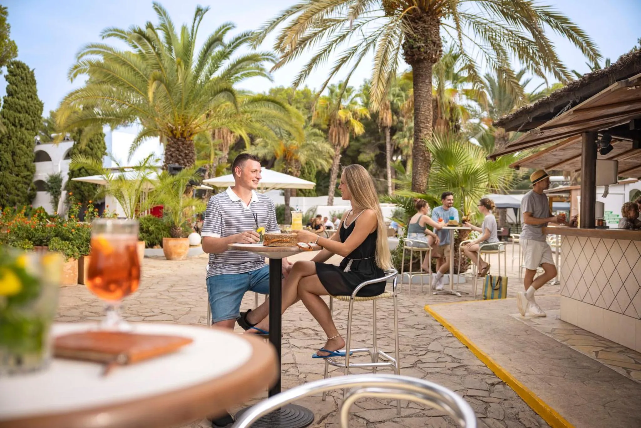 Des clients sont assis à une table de bar en terrasse, profitant de boissons colorées.