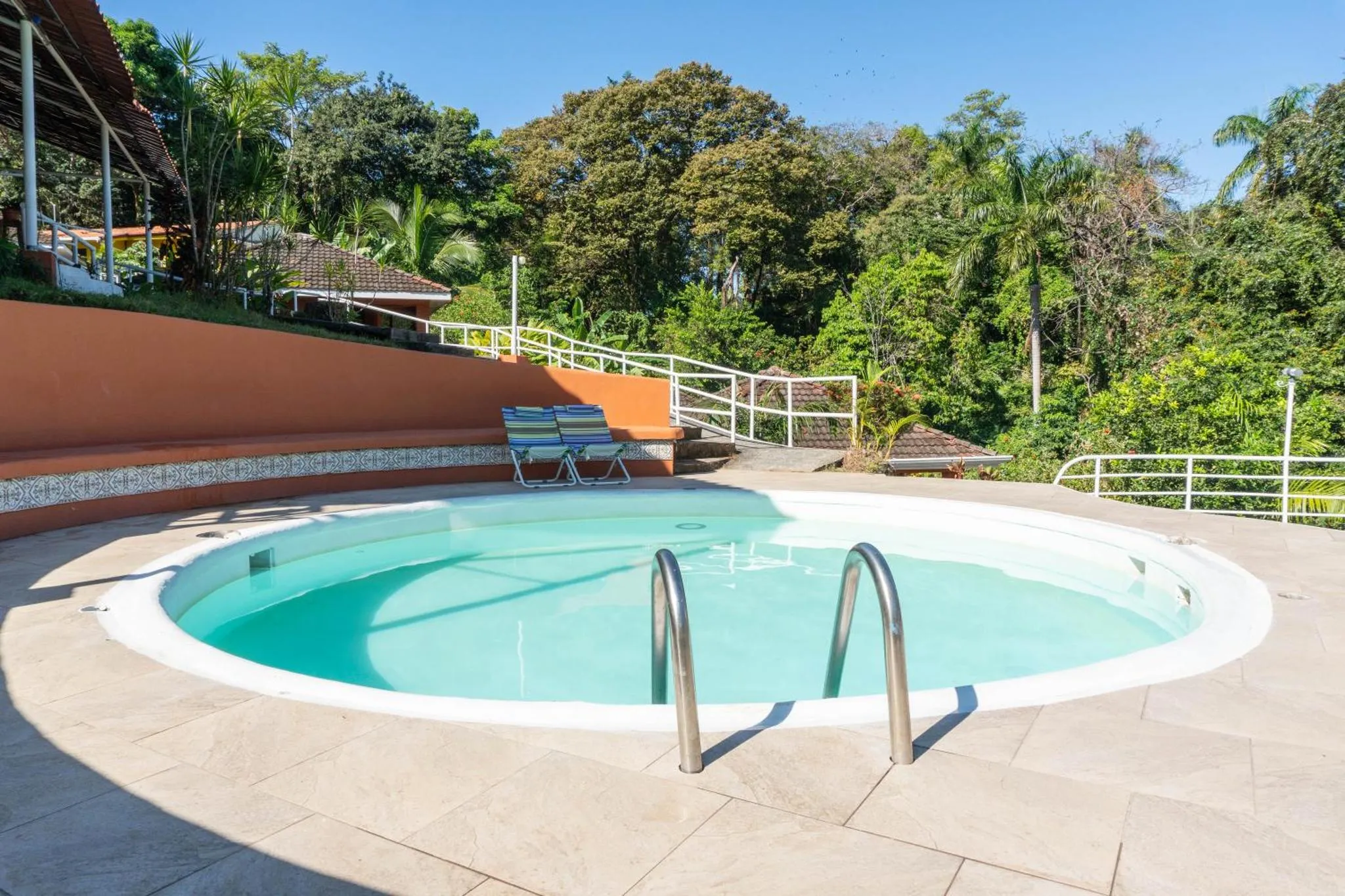 Une piscine circulaire est entourée d'une terrasse ensoleillée et de végétation luxuriante.