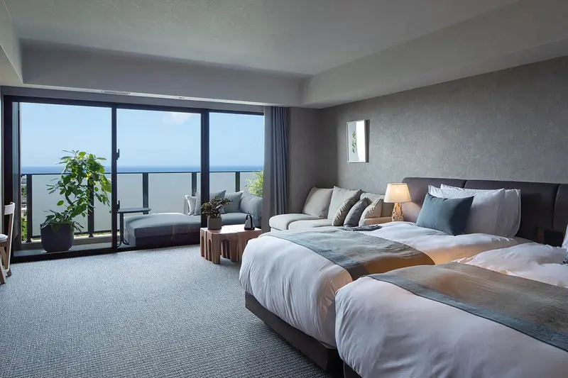 Une chambre spacieuse avec un grand lit et un coin salon donnant sur la mer.