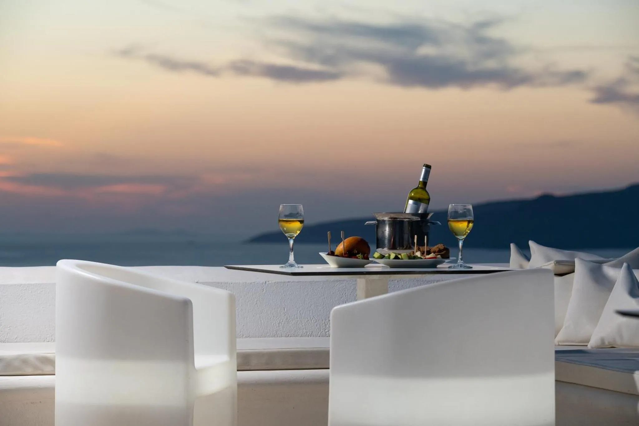 Table dressée avec une bouteille et des verres face à un paysage marin au coucher du soleil.