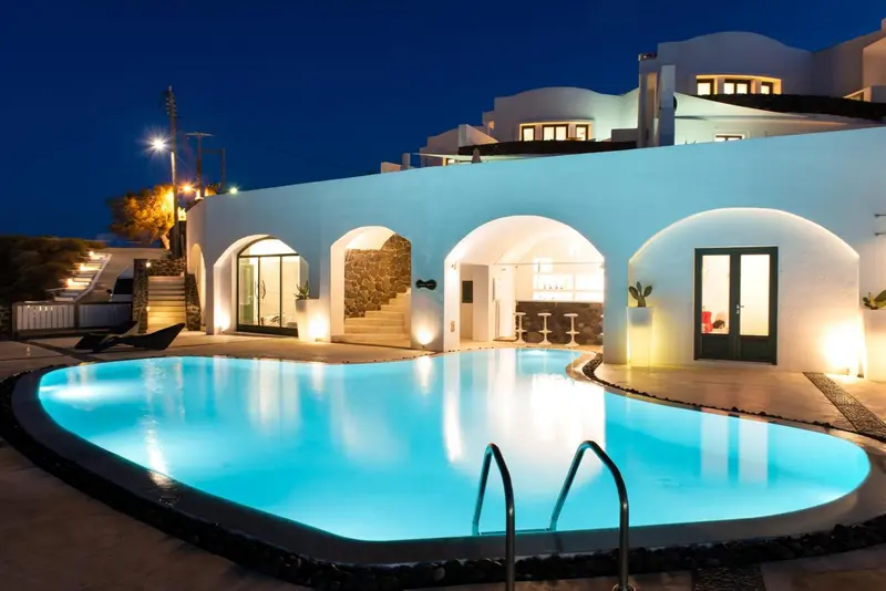 Piscine illuminée devant un bâtiment blanc aux arches.