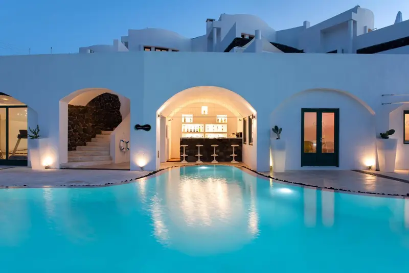 Piscine turquoise devant une architecture blanche aux arches et à l'éclairage tamisé.
