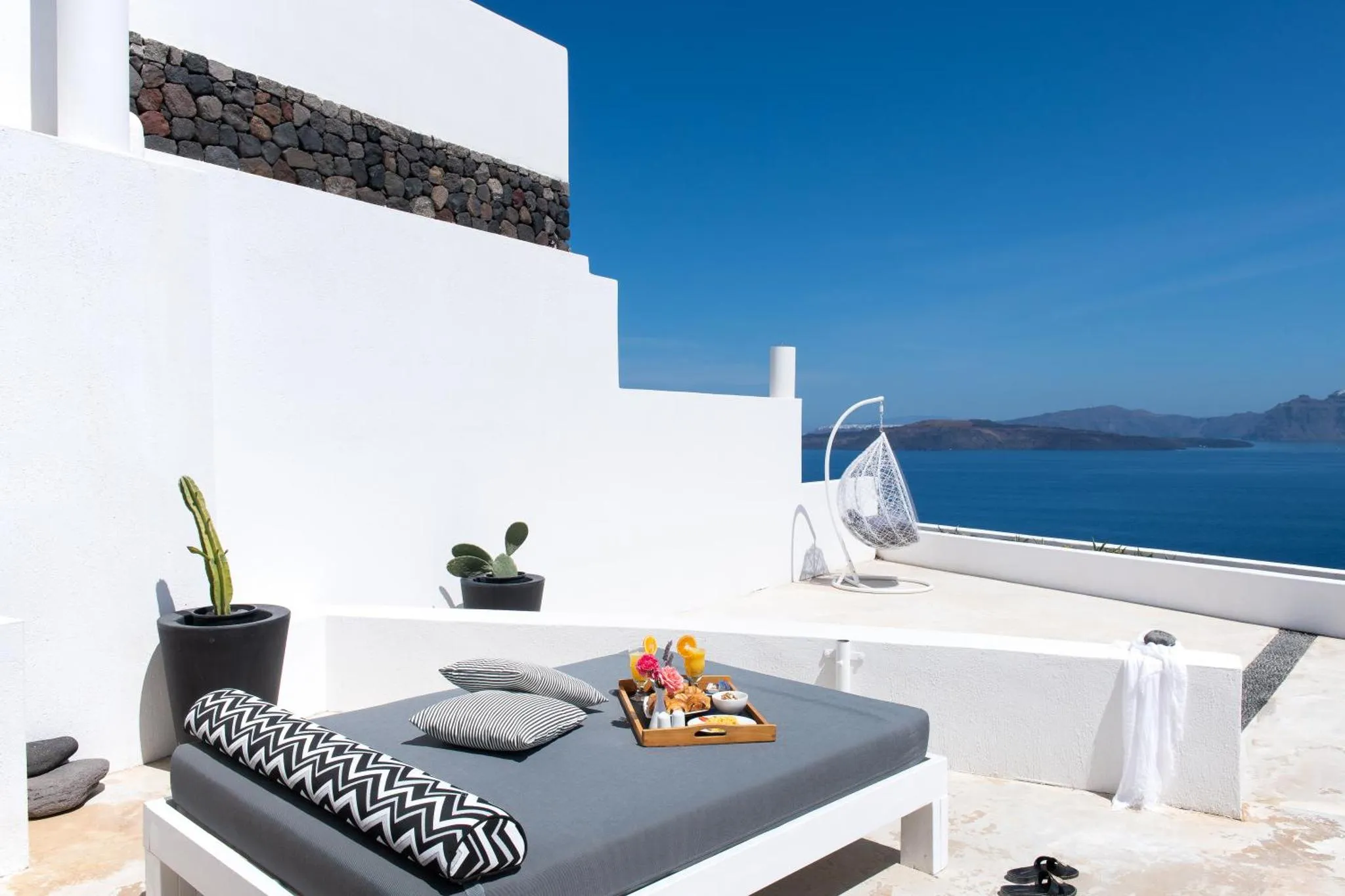 Transats et table basse avec boissons sur une terrasse blanche face à la mer.