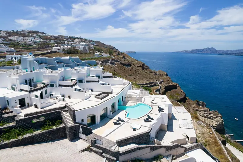 Vue aérienne d'un complexe hôtelier blanc avec piscine à débordement surplombant la mer.
