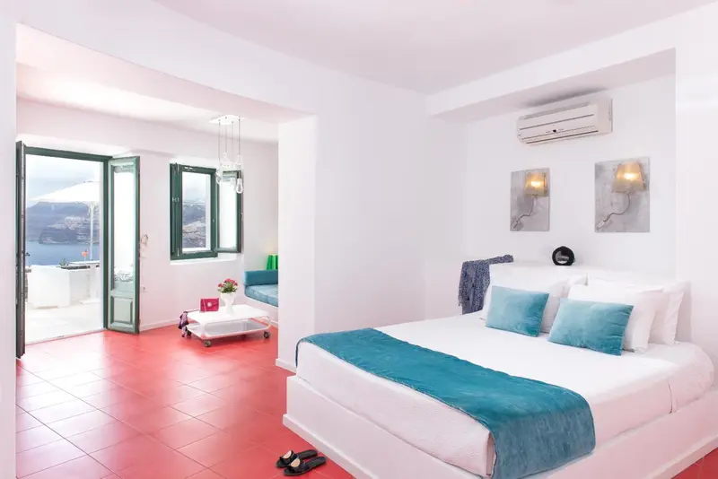 Une chambre lumineuse avec un lit recouvert d'une couverture turquoise et une vue sur la mer.