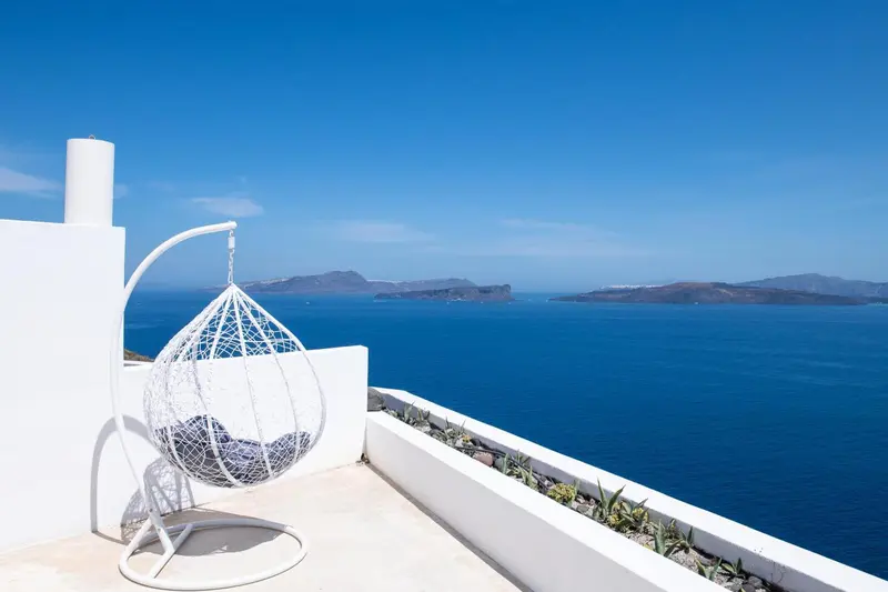 Un fauteuil suspendu blanc offre une vue dégagée sur la mer et les îles au loin.