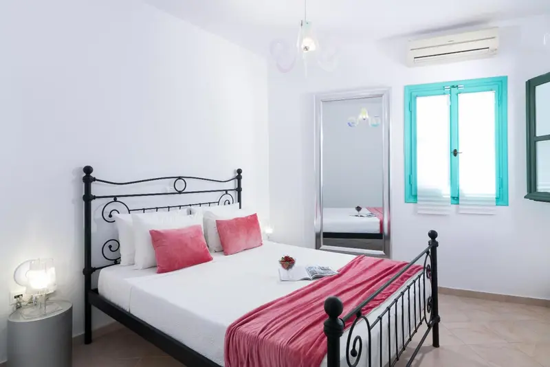 Une chambre lumineuse avec un lit recouvert d'une couverture rose et un miroir.