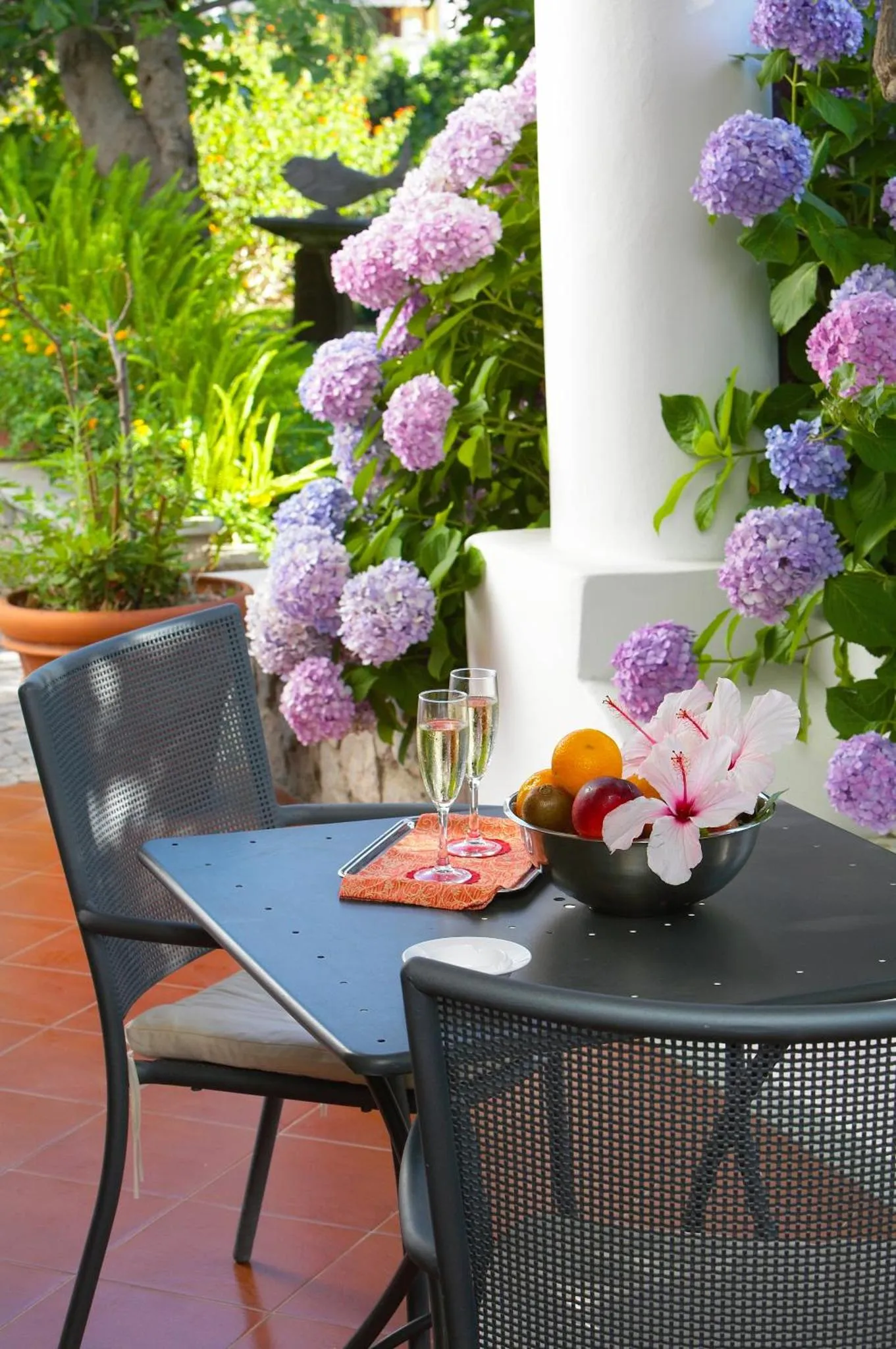 Une table avec des fruits et des boissons sur une terrasse fleurie.