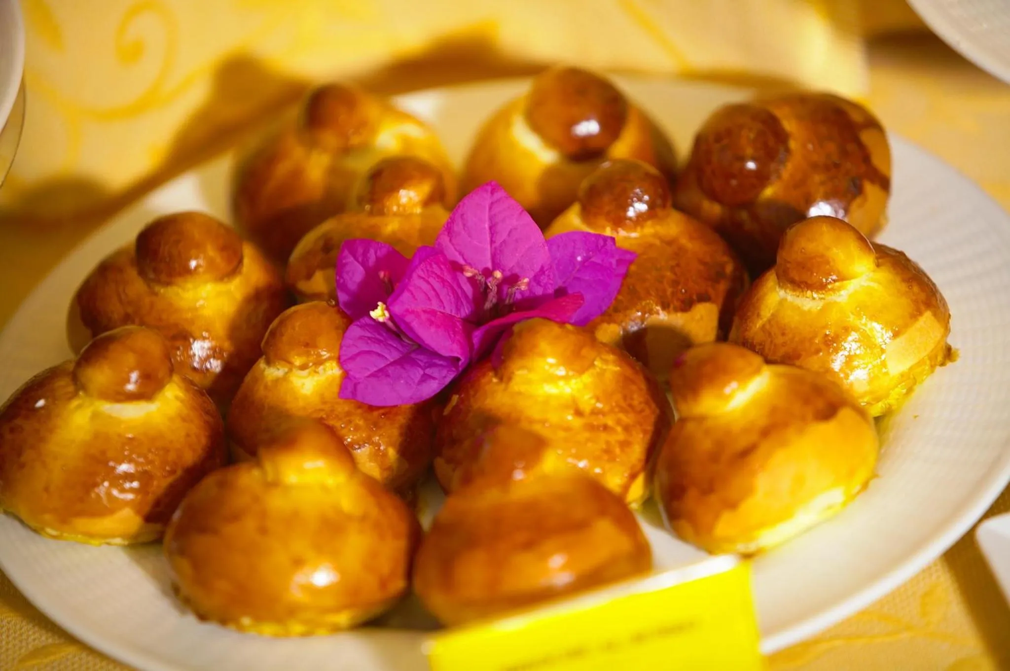 Assortiment de viennoiseries dorées présentées sur une assiette blanche, décorées d'une fleur rose.