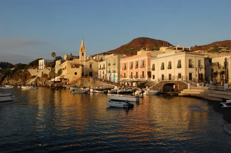 Vue d'un port de plaisance avec des bâtiments colorés et une église au loin.