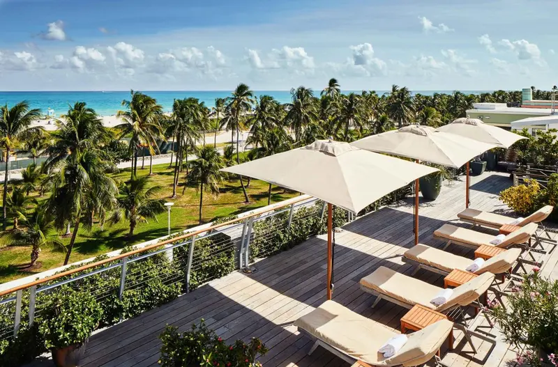 Terrasse en bois avec transats et parasols donnant sur une plage de sable fin et la mer.