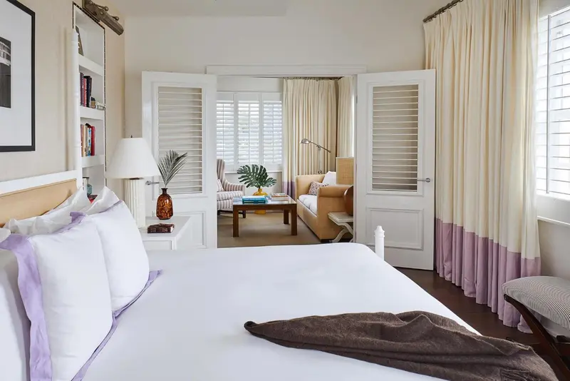 Une chambre lumineuse avec un lit fait et un espace salon attenant.