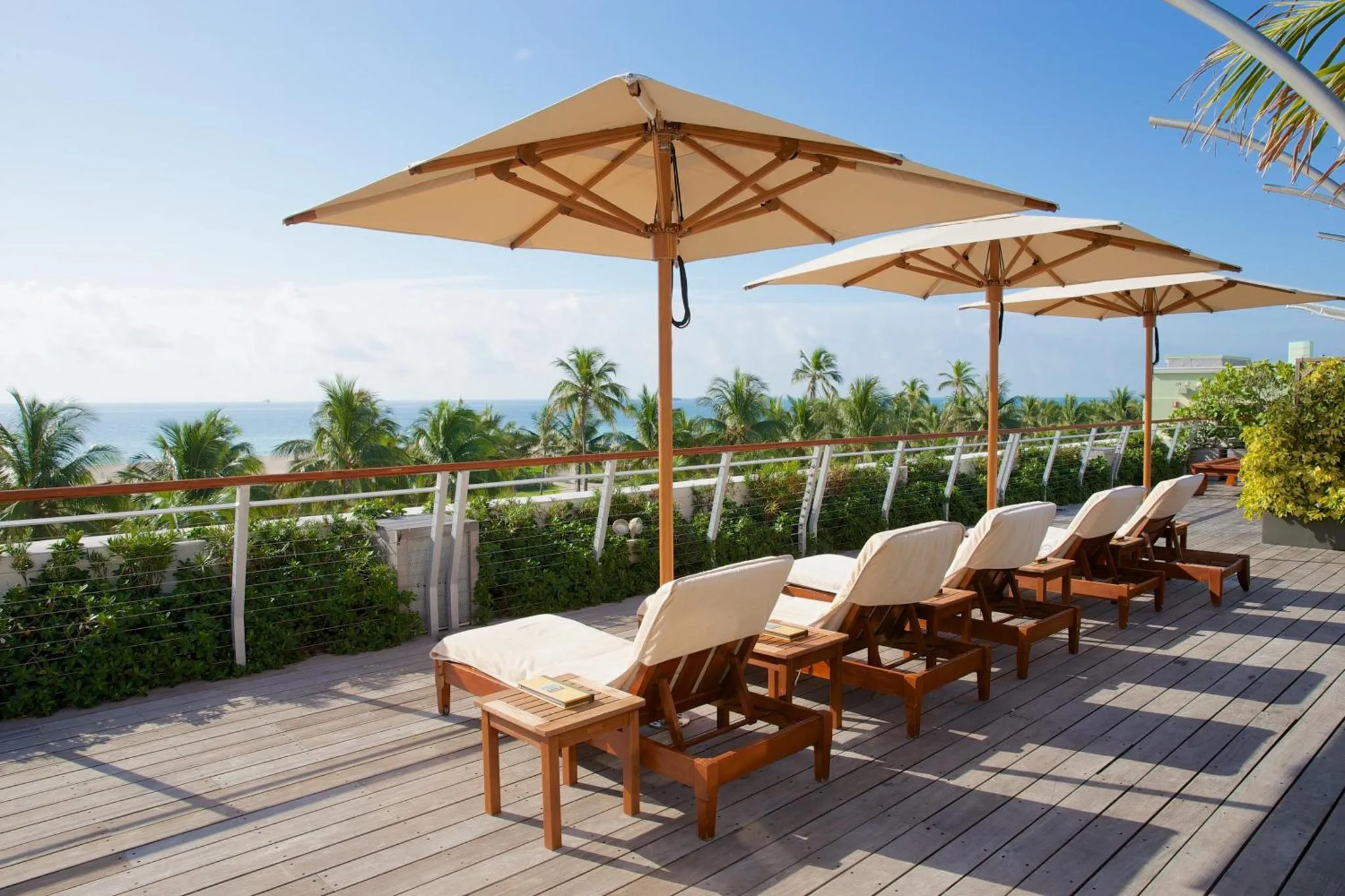 Transats et parasols sur une terrasse en bois avec vue sur la mer et la végétation.