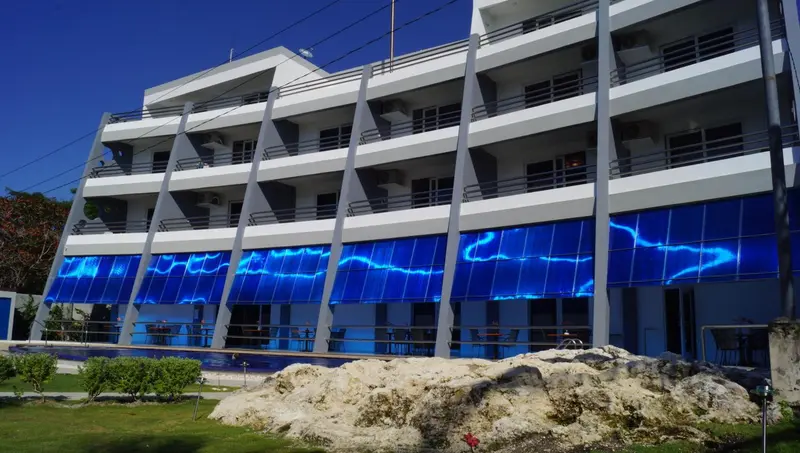 Bâtiment blanc à plusieurs étages avec des balcons et une façade bleue ondulée.