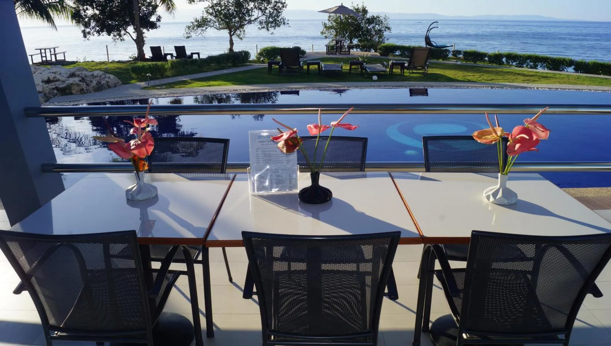 Tables et chaises disposées devant une piscine avec vue sur la mer.