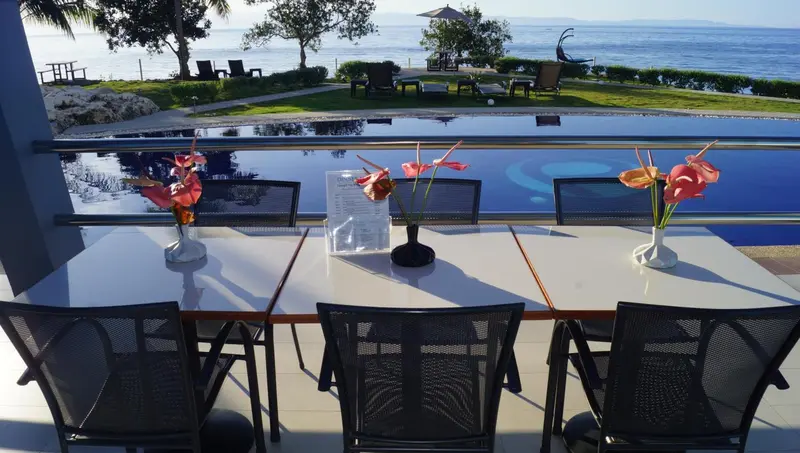 Tables et chaises disposées devant une piscine avec vue sur la mer.