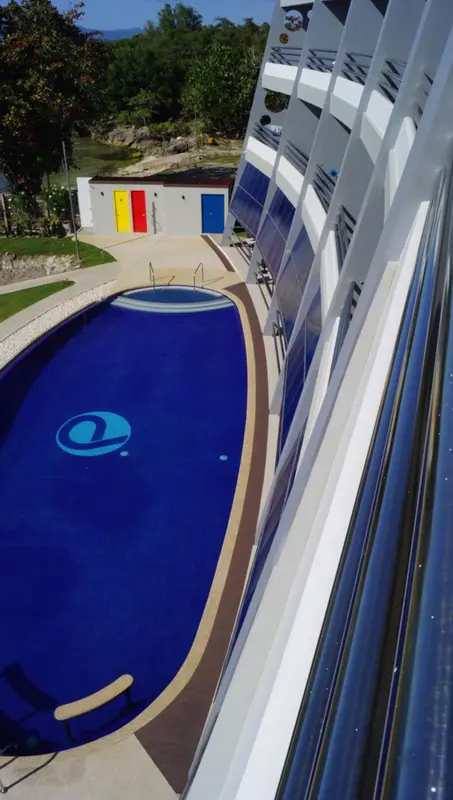 Une piscine rectangulaire bleue avec un logo au centre, entourée d'une terrasse ensoleillée.