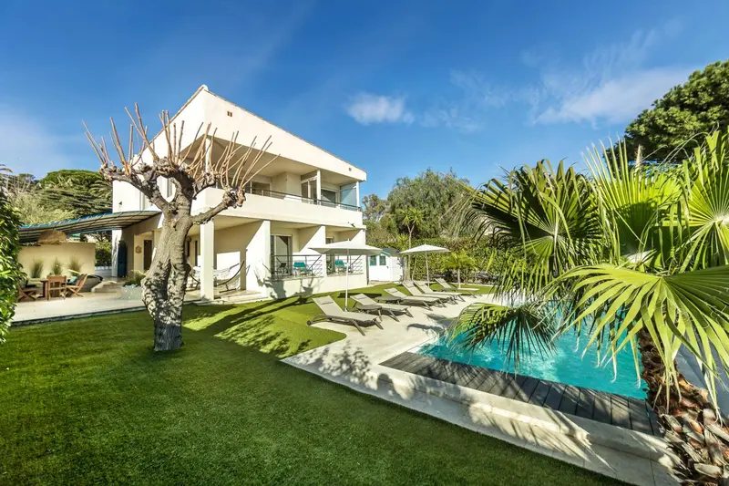 Bâtiment blanc à deux étages entouré d'une végétation luxuriante et d'une piscine.