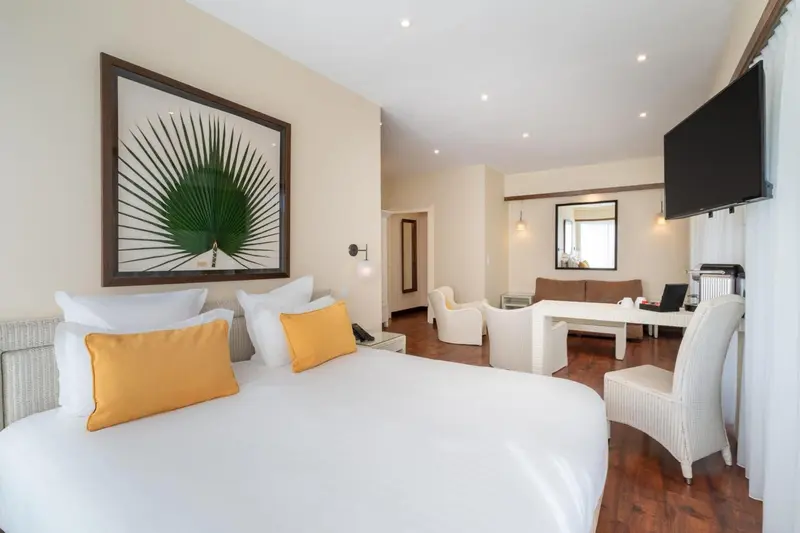 Chambre lumineuse avec un grand lit et un espace salon.