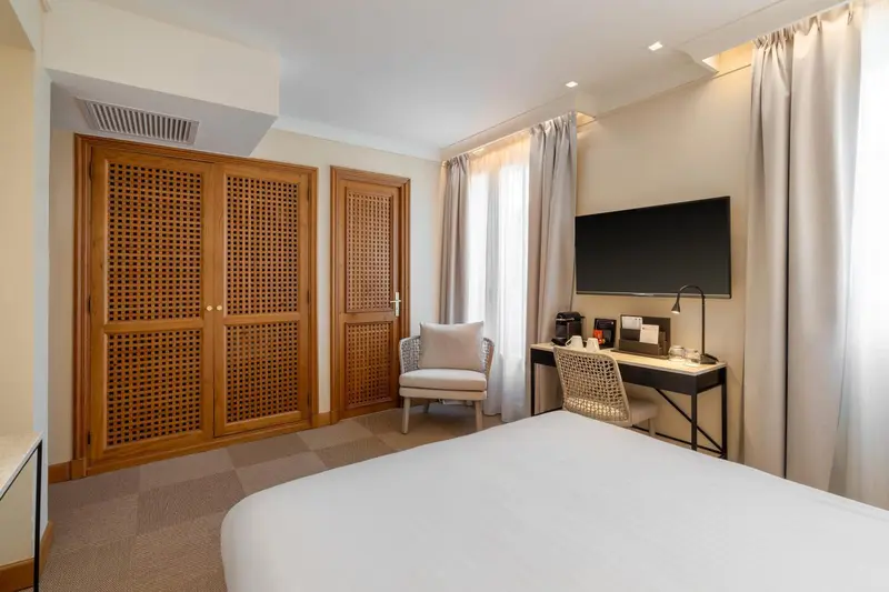 Une chambre d'hôtel lumineuse avec un lit, un bureau et un fauteuil.