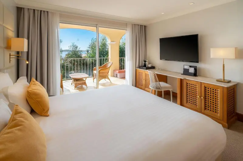 Chambre lumineuse avec un grand lit et une vue sur la mer depuis un balcon.