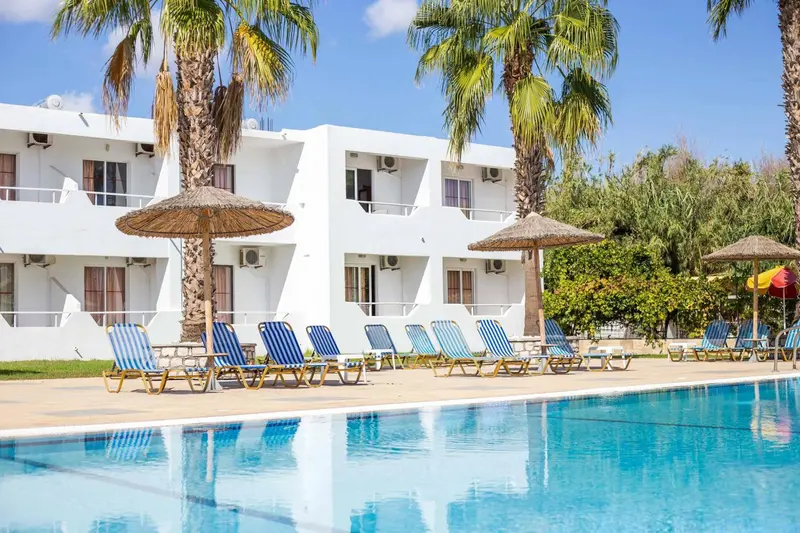 Bâtiment blanc à deux étages avec des transats bleus près d'une piscine.