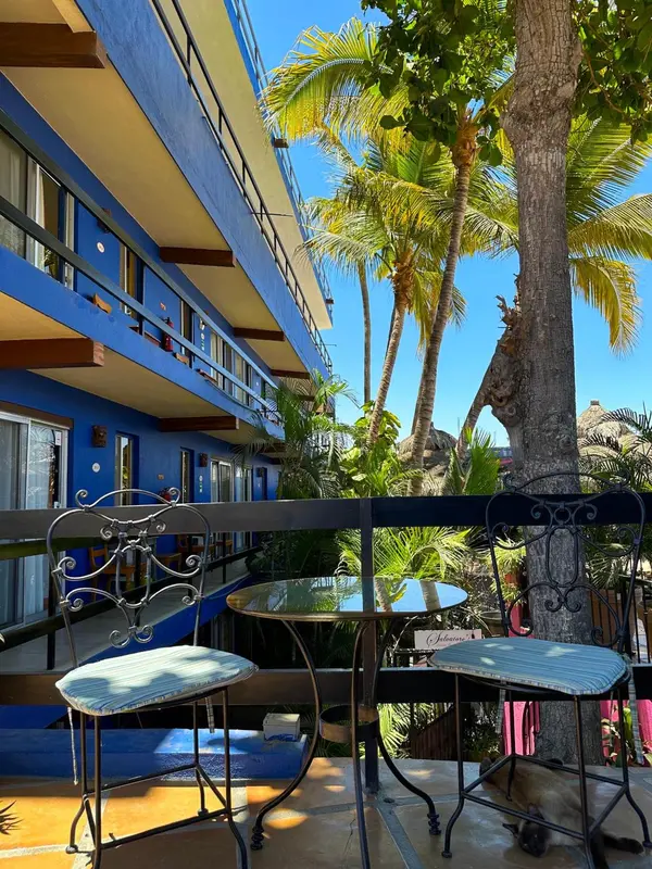 Terrasse avec mobilier en fer forgé devant un bâtiment bleu et des palmiers.