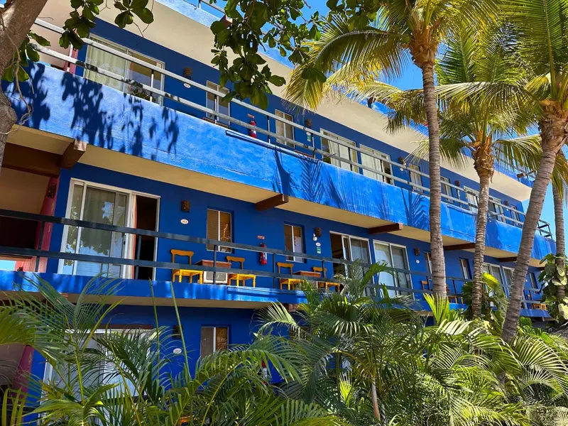 Bâtiment bleu à balcons, entouré de végétation tropicale sous un ciel clair.