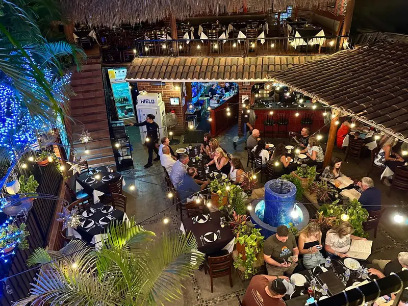Une terrasse éclairée accueille des convives autour de tables.