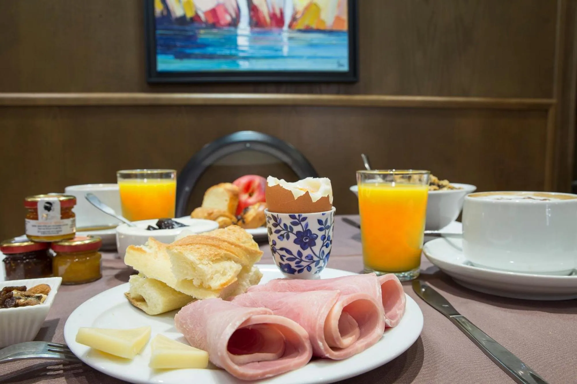 Une table est dressée avec un petit-déjeuner composé de viennoiseries, de charcuterie et de boissons.