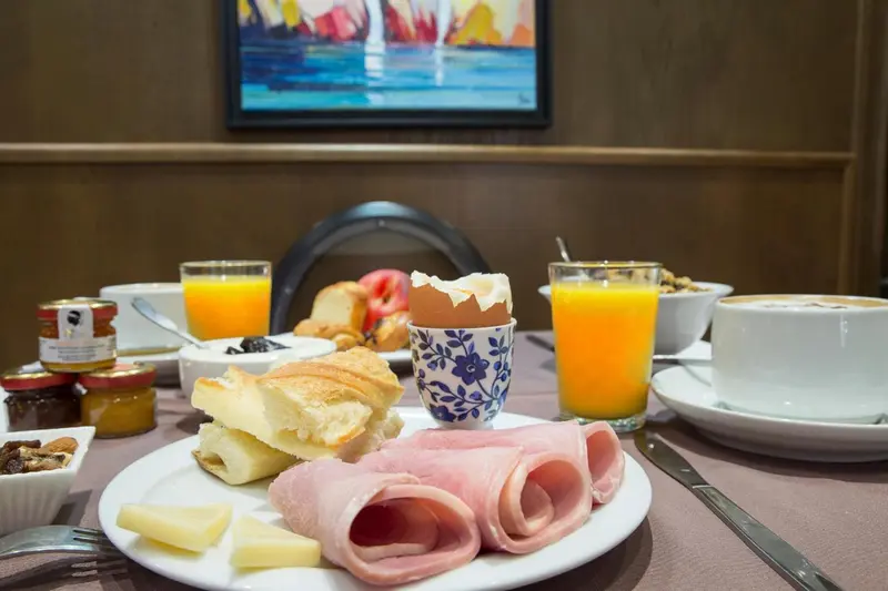 Une table est dressée avec un petit-déjeuner composé de viennoiseries, de charcuterie et de boissons.