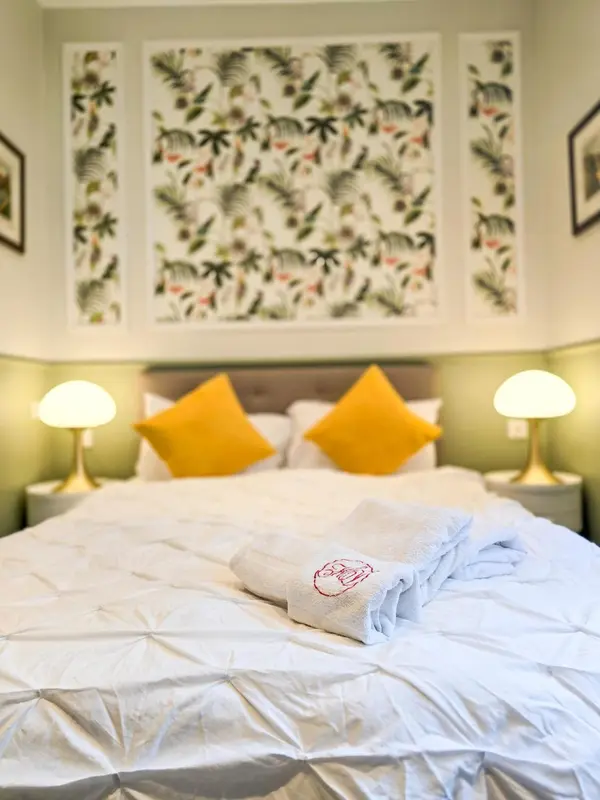 Un lit blanc avec des oreillers jaunes et des lampes de chevet dorées dans une chambre.