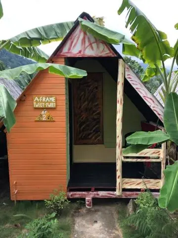 Petite cabane en bois orange avec un toit rouge et blanc, entourée de végétation.