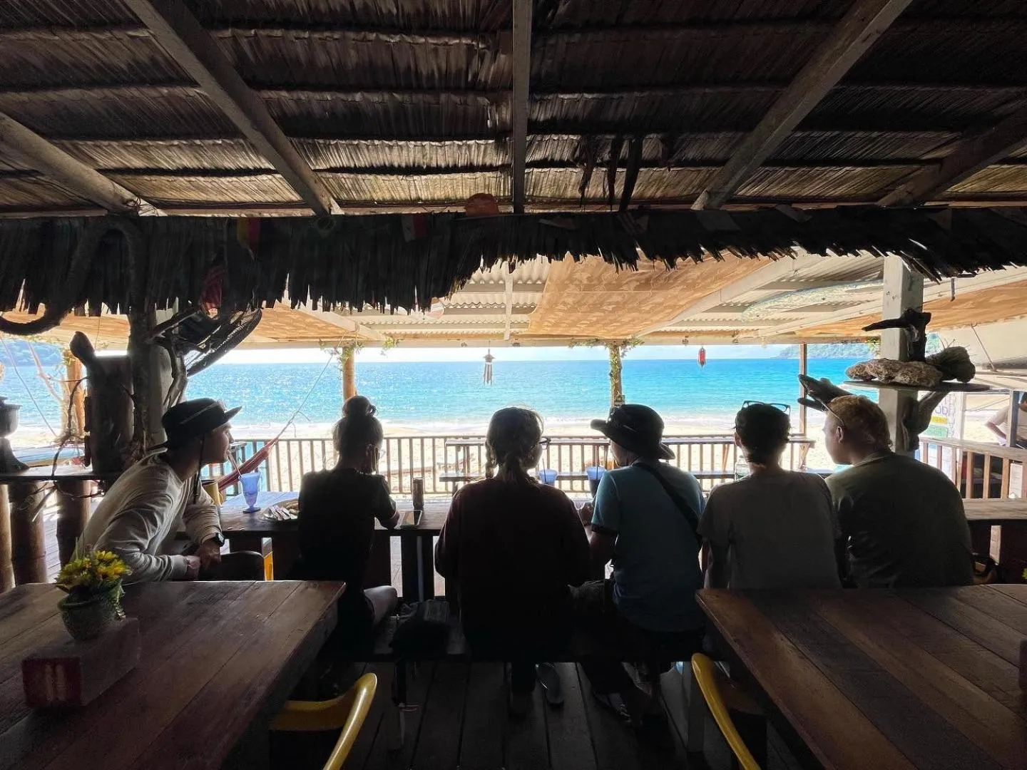 Des personnes sont assises à une table en bois face à la mer.
