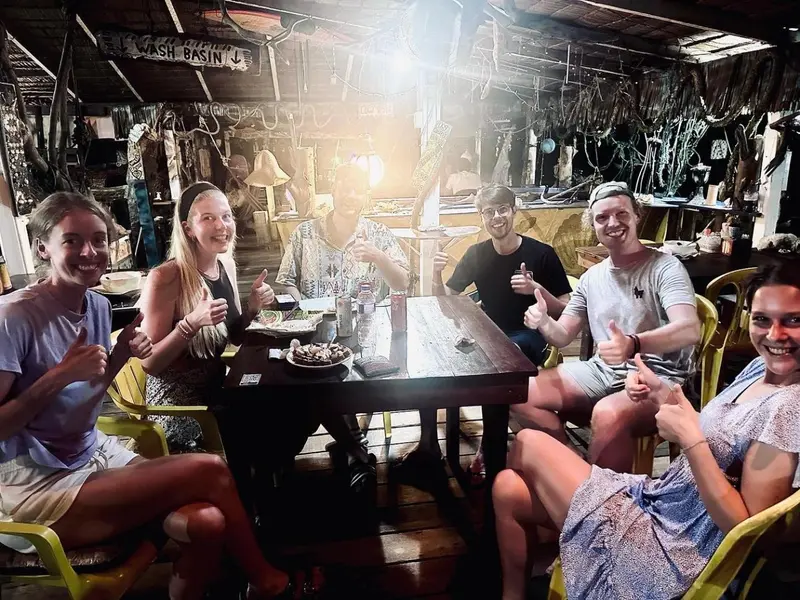 Des convives sourient et lèvent leurs pouces en l'air autour d'une table dans un espace de restauration en plein air.