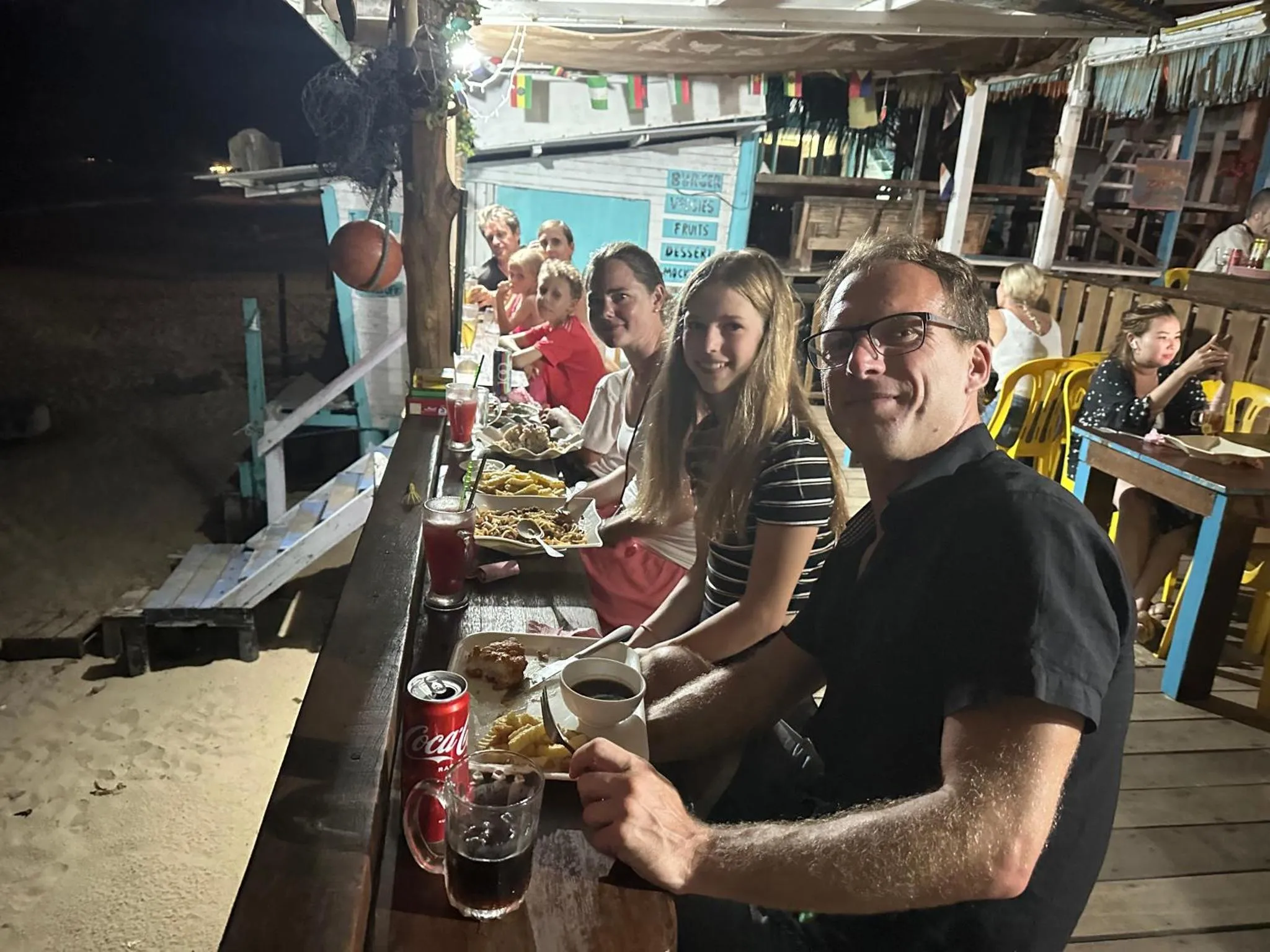 Une famille souriante est assise à une table en plein air devant un restaurant.