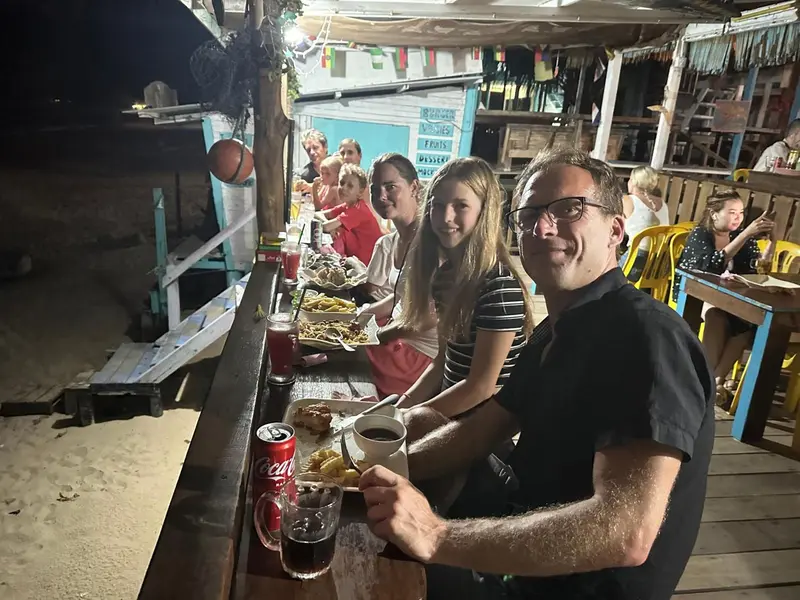 Une famille souriante est assise à une table en plein air devant un restaurant.