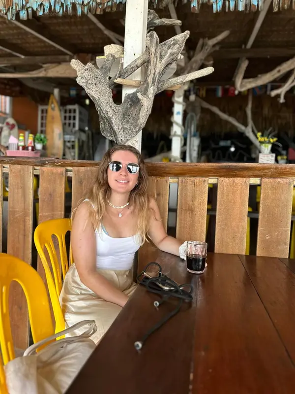 Une personne assise à une table en bois dans un espace extérieur ombragé.