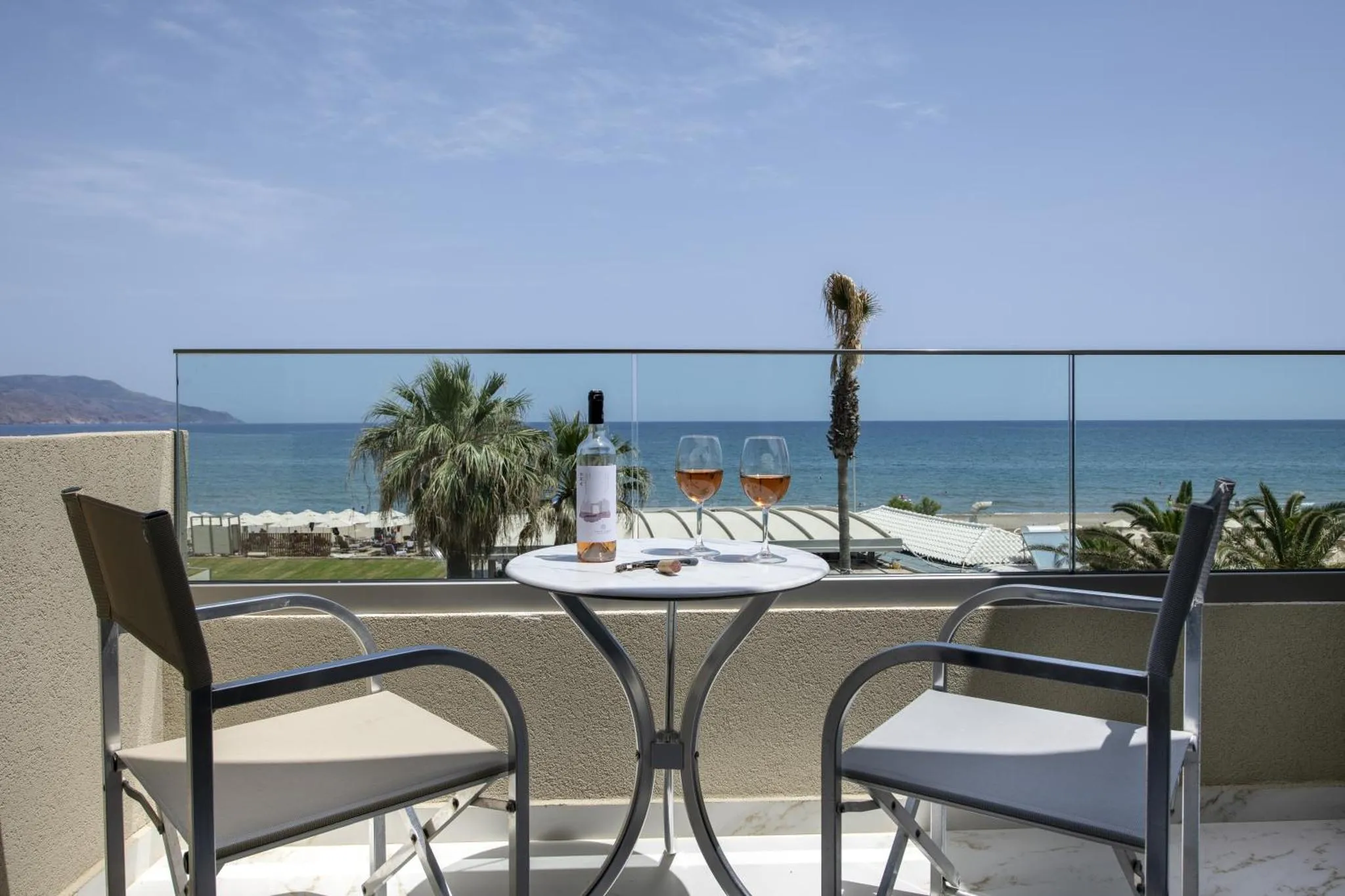 Une table avec une bouteille et deux verres sur une terrasse ensoleillée avec vue sur la mer.