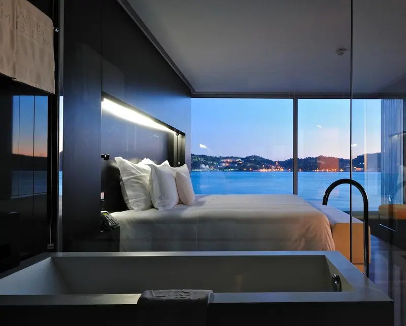 Une chambre avec un grand lit face à une baie vitrée donnant sur la mer.