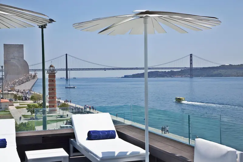 Terrasse avec transats blancs et vue sur un pont et la mer.