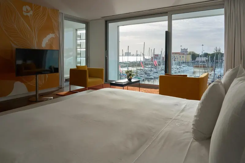 Chambre lumineuse avec un grand lit et vue sur un port de plaisance.