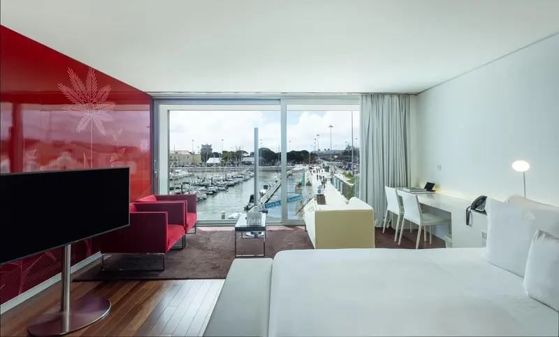 Une chambre lumineuse avec un grand lit et un coin salon donnant sur un port de plaisance.