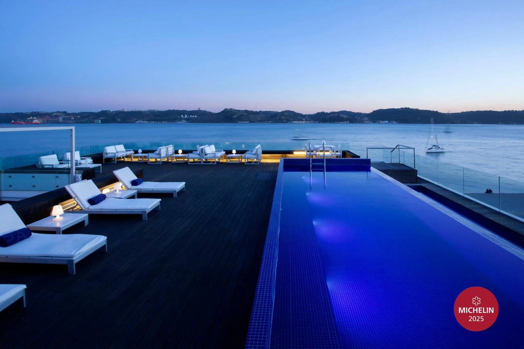 Terrasse avec piscine et transats au bord de la mer au coucher du soleil.